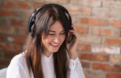 Femme souriante portant un casque audio, devant un mur en briques.