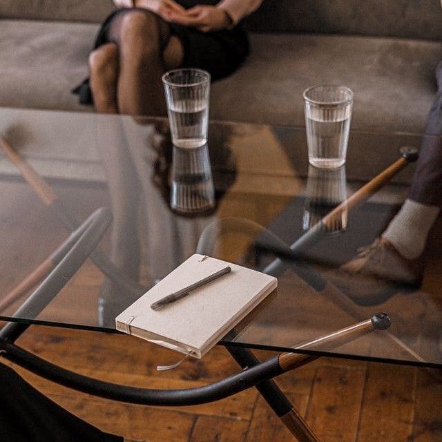 Un carnet et un stylo sur une table en verre, avec deux verres d'eau et des personnes assises.