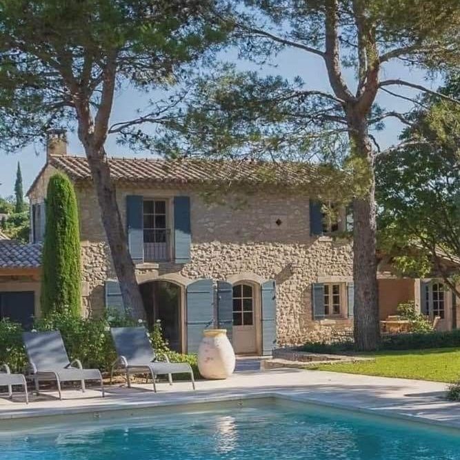 Maison en pierre avec piscine, jardin et arbres, dans un cadre ensoleillé.